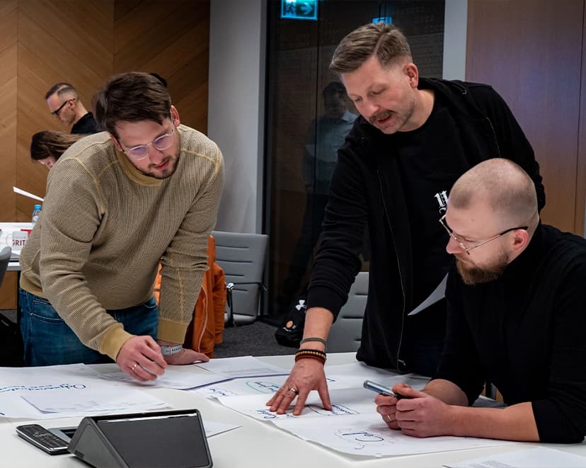 Three developers discuss the project, papers on the desk