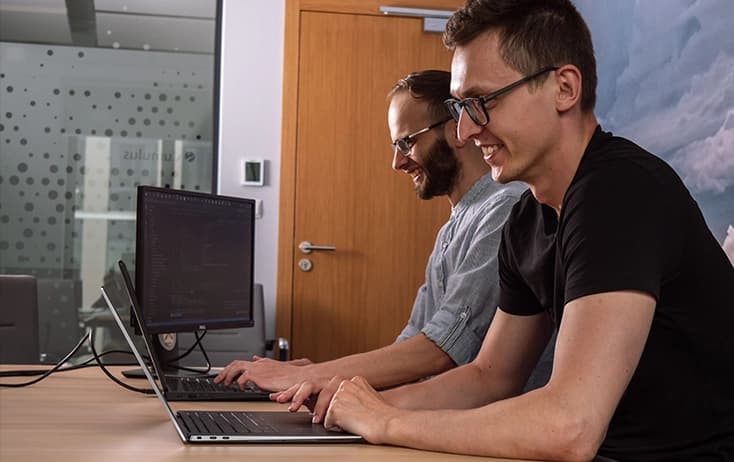 Two developers working on their laptops and smiling.