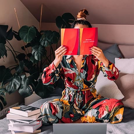 A girl sitting on the couch reading a notebook with "Agile Soul" cover.